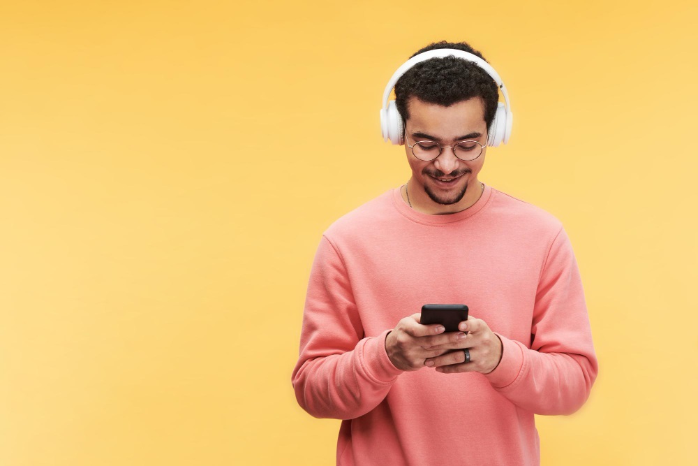 happy guy headphones eyeglasses pink sweatshirt using smartphone s